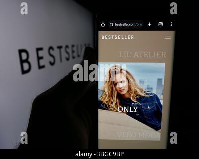 Dans cette illustration photo, une personne tient un téléphone portable avec la page Web de la société de vêtements danois Bestseller COMME sur l'écran devant le logo. Banque D'Images