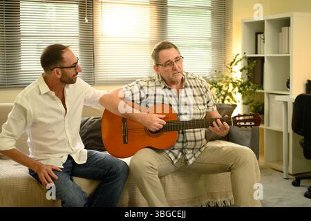Père et fils adultes se liant sur la musique, appréciant le temps de qualité avec guitare acoustique. Concept de fête des pères Banque D'Images