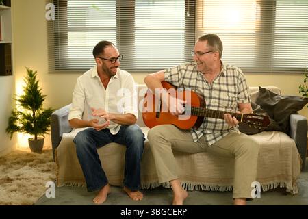 Père et fils adultes se liant sur la musique, appréciant le temps de qualité avec guitare acoustique. Concept de fête des pères Banque D'Images