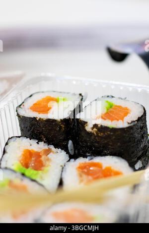 Voici une image détaillée en gros plan de délicieux rouleaux de sushi placés soigneusement à l'intérieur d'un récipient en plastique transparent, à côté d'une paire de baguettes pour une main facile Banque D'Images