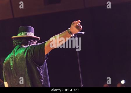 Chanteur portant un chapeau élégant et gilet, étendant un bras tout en se produisant passionnément sur scène avec un microphone, captivant le public Banque D'Images