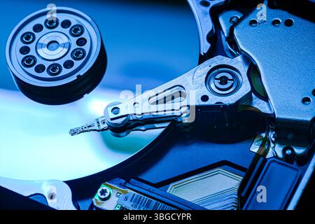 Gros plan des éléments internes du disque dur baignés de lumière bleue, montrant la tête de lecture/écriture qui analyse activement le plateau Banque D'Images