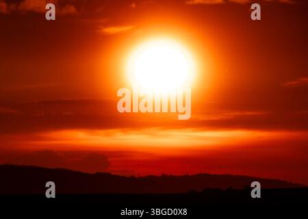 Coucher de soleil ardent avec un soleil intense et brillant sur des collines sombres lointaines, véhiculant chaleur, puissance et drame atmosphérique Banque D'Images