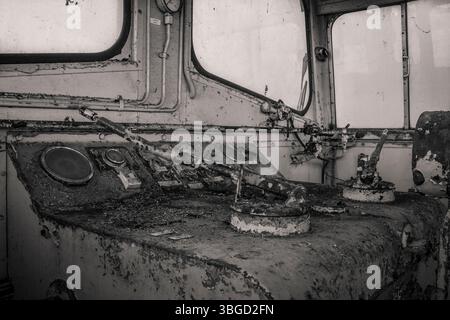 Gros plan des leviers rouillés et du panneau de commande à l'intérieur d'une cabine de train abandonnée, mettant en évidence la décomposition, la négligence et le passage du temps Banque D'Images