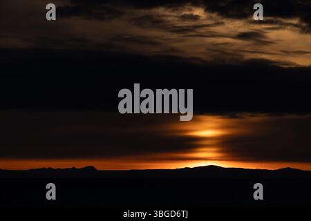 Coucher de soleil spectaculaire sur la côte silhouette dans le détroit de Davis, au Groenland, avec des nuages en couches et une lueur orange dans le ciel arctique. Banque D'Images