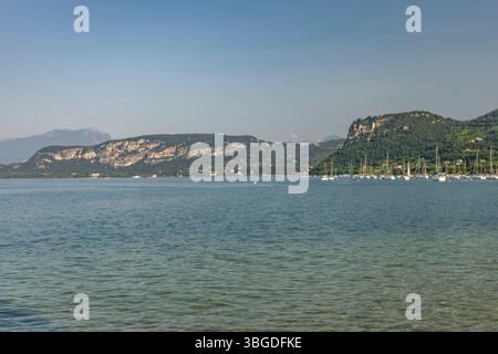 Lac de Garde, Italie 3 janvier 2025 : paysage tranquille du lac de garde avec des voiliers amarrés près de la rive, encadrés par des montagnes pittoresques et le charmin Banque D'Images