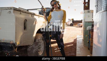 Femme portant des lunettes de soleil, chemise à carreaux tenant la buse de pompe, posant par camion utilitaire à la station-service Banque D'Images