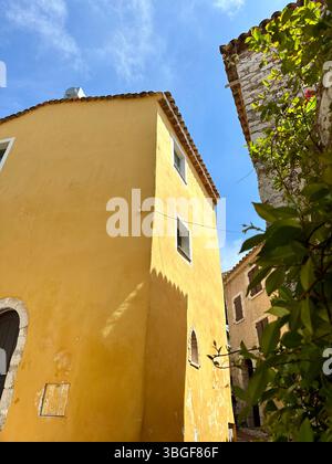 Bâtiment en stuc jaune à Èze, en France, encadré par des branches verdoyantes et un ciel bleu, capturant le charme méditerranéen et la chaleur architecturale. Banque D'Images