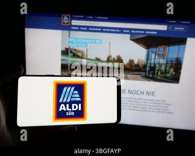 Stuttgart, Allemagne - 03-13-03 2025 : personne tenant un smartphone avec le logo de la société allemande ALDI SÜD sur l'écran devant le site Web de l'entreprise. Banque D'Images
