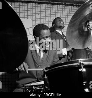 Der US-amerikanische Jazzschlagzeuger Buster Smith (vorn am Schlagzeug) und der bassiste George Joyner (im Hintergrund) BEI einem mitreißenden Live-Konzert in einem Club der 1960er Jahre. Beide Musiker sind im moment des Spiels vertieft, die Energie des Jazz ist spürbar. Banque D'Images