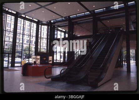 Photographie en couleur de la réception intérieure de la BancOhio National Bank, représentant un escalier roulant avec un homme descendant. Un garde de sécurité est visible à la réception pendant que la réceptionniste le regarde. Le bâtiment, achevé en 1976, est également connu sous le nom de BancOhio National Plaza. Banque D'Images
