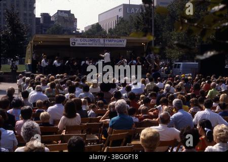 Une photographie d'octobre 1980 montre un chef d'orchestre dirigeant l'Orchestre symphonique de Columbus lors d'un concert en plein air sur la pelouse de l'Ohio Statehouse. Le spectacle est parrainé par diverses organisations, dont le Greater Columbus Arts Council et l'Ohio Arts Council. La vue fait face à State Street et South High Street, avec une vue partielle sur le grand magasin Lazarus et une publicité pour les cigarettes Marlboro. Banque D'Images