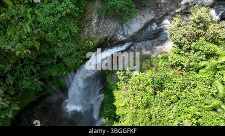 Cette prise de vue aérienne capture la cascade de Tiu Kelep qui traverse des falaises rocheuses et une jungle dense, mettant en évidence le contraste spectaculaire entre l'eau et le RA Banque D'Images