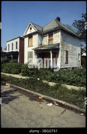 Une maison à ossature de bois de deux étages non identifiée est vacante ou abandonnée. Il est arboré avec des fenêtres cassées et des dommages visibles par le feu sur l'avant-toit. La propriété apparaît délabrée et vide. Banque D'Images
