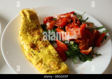 Petit déjeuner sain avec omelette et salade fraîche avec tomates cerises et roquette, habillé avec moutarde, miel et sauce à l'huile d'olive sur assiette blanche. Nutr Banque D'Images