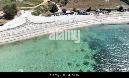 Gros plan d'une plage de sable blanc immaculé sur Lombok avec une eau turquoise claire. Parasols et petites cabanes invitent à une escapade tropicale relaxante. Banque D'Images