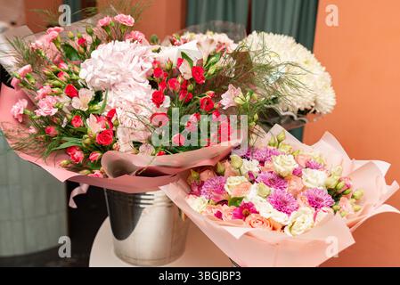 Beaux bouquets de fleurs mélangées avec des roses, des œillets et des chrysanthèmes dans un emballage rose, parfait pour des cadeaux, des événements ou un décor. Banque D'Images