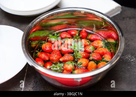 Fraises rouge vif lavées dans un bol en métal rempli d'eau, préparées pour un dessert, une collation ou une recette. Banque D'Images