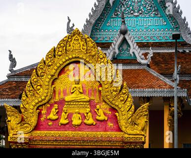 Une façade vibrante de temple avec des sculptures complexes dorées et roses de Bouddha et d'autres personnages, sur fond d'un temple asiatique traditionnel Banque D'Images