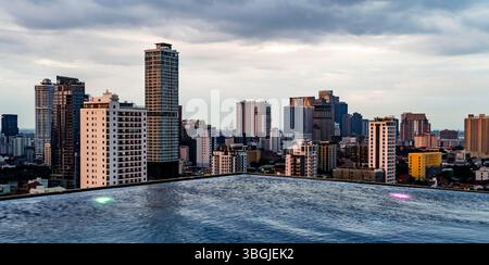 Une vue panoramique sur les gratte-ciel modernes de la ville avec de hauts bâtiments et gratte-ciel sous un ciel nuageux. Une piscine à débordement est visible au premier plan, Banque D'Images
