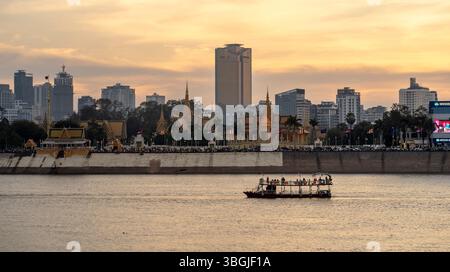 Une vue panoramique sur une rivière au coucher du soleil, avec un bateau au premier plan et une ligne d'horizon de la ville en arrière-plan. L'horizon comprend des bâtiments modernes et Banque D'Images