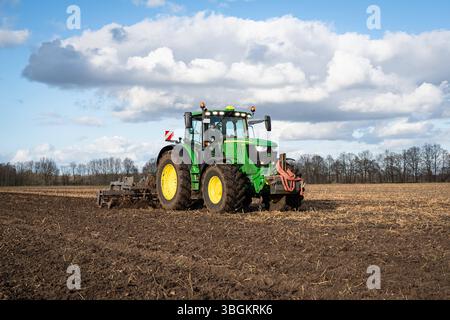 Ackerbau - John Deere 6215R Traktor BEI der Einarbeitung von frisch ausgebrachter Gülle in den Boden. Gülleausbringung und kurzfristige Einarbeitung mit GRubber und Nachlaufwalze in den Boden, um Geruchsimmisionen und Nährstoffverluste zu vermeiden. Praxisfoto aus der Landwirtschaft. Landkreis Diepholz Niedersachsen Deutschland *** culture arable John Deere 6215R tracteur incorporant du fumier fraîchement appliqué dans le sol application de fumier liquide et incorporation à court terme dans le sol avec un cultivateur et un rouleau traînant pour éviter les immissions d'odeur et les pertes de nutriments photo pratique Banque D'Images