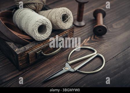 Outils et accessoires pour l'artisanat ou l'emballage cadeau : ciseaux de bonsaï, corde de jute, ruban de cuir et bobines dans une boîte en bois vintage sur BA en bois foncé Banque D'Images