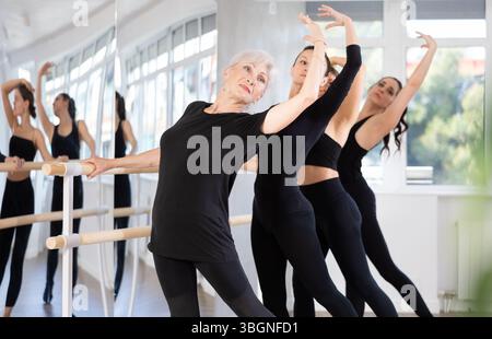 Femme âgée exécutant un tendu de combat à la barre pendant la répétition de groupe Banque D'Images