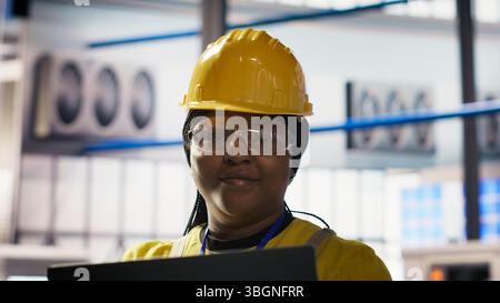 Smiling Smart Factory spécialiste teste les systèmes automatisés pour assurer la fiabilité. Ingénieur heureux dans l'industrie 4,0 usine industrielle identifier les goulets d'étranglement et optimiser les engrenages en fonction des données, caméra B. Banque D'Images