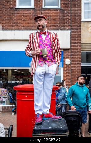 Un homme habillé de couleurs vives se tient sur Une poubelle à litière pour Une meilleure vue d'Un groupe d'artistes de rue du jour de mai, High Street, Lewes, East Sussex, Royaume-Uni. Banque D'Images