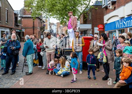 Un homme habillé de couleurs vives se tient sur Une poubelle à litière pour Une meilleure vue d'Un groupe d'artistes de rue du jour de mai, High Street, Lewes, East Sussex, Royaume-Uni. Banque D'Images