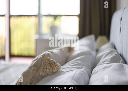 Intérieur confortable de la chambre, couvre-lit beige et oreiller, lampe de chevet à côté du lit, lumière de la fenêtre Banque D'Images