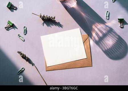 Composition minimaliste à plat avec carte vierge, enveloppe brune, lavande et papeterie à la lumière naturelle. Vue de dessus, maquette Banque D'Images