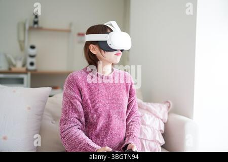 Dans une pièce propre et ensoleillée avec un éclairage doux, une femme japonaise enceinte dans la vingtaine avec les cheveux bruns courts, vêtue d'une robe en tricot rose, s'assoit Banque D'Images