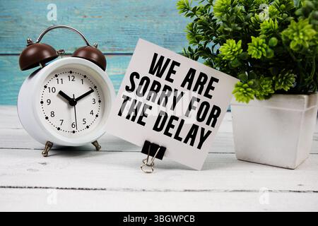 Nous sommes désolés pour le texte de retard écrit sur carte papier avec réveil sur fond en bois Banque D'Images