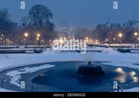 Prise de vue matinale en début d'hiver du parc Ambiorix enneigé de Bruxelles, avec un étang gelé et une fontaine Banque D'Images
