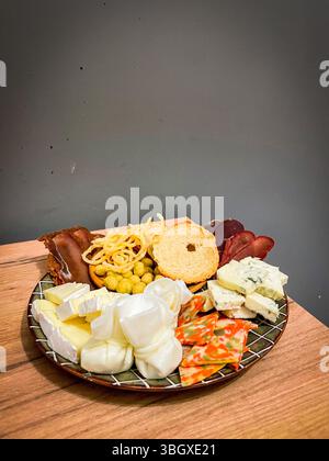 Plateau de fromage gastronomique assorti avec brie, bleu, mozzarella, tranches colorées, charcuterie, et des collations croquantes disposées sur une assiette rustique pour la dégustation Banque D'Images