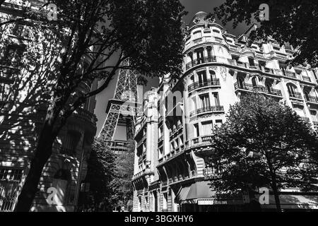 Un cliché spectaculaire en noir et blanc regardant depuis une rue parisienne, capturant la Tour Eiffel au milieu de bâtiments classiques, d'arbres et d'un panneau « HOTEL CAFE » Banque D'Images