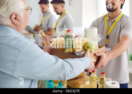 Homme volontaire donnant une boîte de nourriture à un homme âgé au centre d'aide Banque D'Images