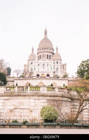 Une vue frontale d'une grande basilique en pierre blanche avec plusieurs dômes, située sur une colline. De larges marches en pierre et terrasses mènent à l'entrée, avec p Banque D'Images