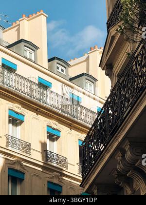 La façade d'un immeuble parisien ensoleillé présente une architecture classique, des lucarnes, des balcons en fer forgé et des auvents bleu vif sur certains Banque D'Images