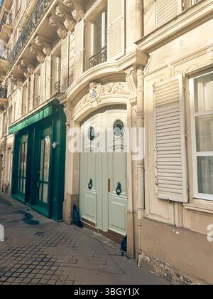 Une charmante façade de bâtiment parisien avec une double porte blanche avec des détails ornés et une façade verte à côté, baignée de soleil sur une ville s. Banque D'Images