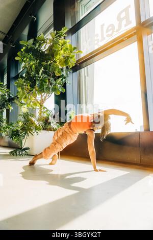 Femme en planche latérale pose à l'intérieur avec des plantes et la lumière du soleil Banque D'Images