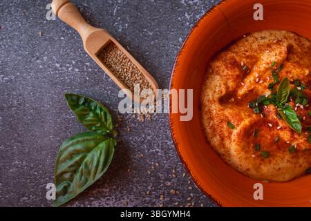 Houmous décoré d'herbes et de graines de sésame dans un bol orange Banque D'Images