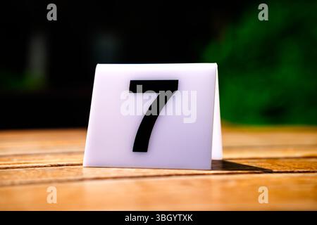 Un support de numéro de table affichant le chiffre 7 est assis sur une table en bois, prêt à identifier un emplacement de siège spécifique pour les clients ou les invités dans un restau Banque D'Images