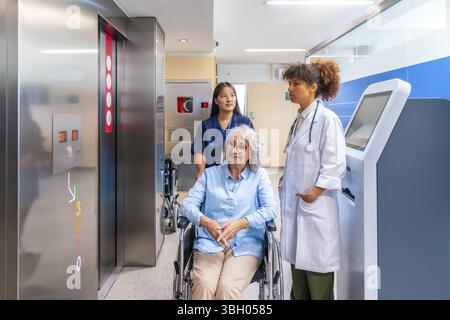 Professionnels de la santé qui fournissent des soins et du soutien à une femme âgée en fauteuil roulant, naviguant dans un environnement hospitalier moderne Banque D'Images