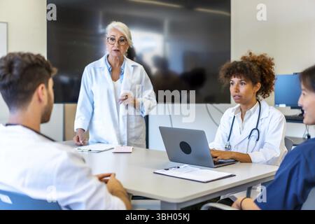 Médecins et professionnels de la santé collaborant, partageant leur expertise et analysant les informations des patients lors d’une réunion productive dans un hôpital moderne Banque D'Images