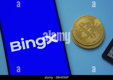 Logo BingX sur l'écran du smartphone près de Bitcoin coin et QR code sur fond bleu Banque D'Images