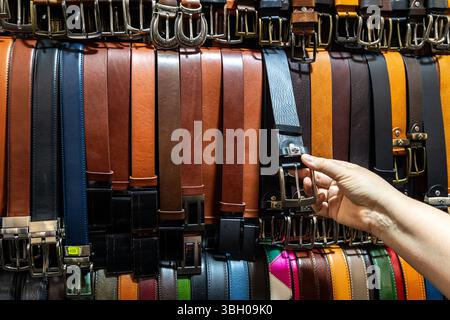 Florence, Italie - 10 mai 2025 : un client ramasse une ceinture en cuir dans un étal coloré du marché au Mercato Nuovo Banque D'Images