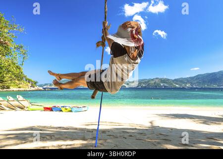 Femme heureuse avec un short, une chemise et un chapeau à large bord balançant à Paradise Beach, la plage la plus célèbre de Patong, Phuket, Thaïlande. Sur fond bleu Banque D'Images